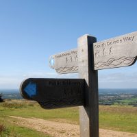 South Downs National Park, Sussex, England, UK. A man and a woman walking on the South Downs way in Sussex. A signpost shows the route of the South Downs Way and views over the Sussex Weald.