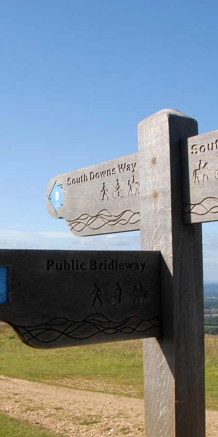 South Downs National Park, Sussex, England, UK. A man and a woman walking on the South Downs way in Sussex. A signpost shows the route of the South Downs Way and views over the Sussex Weald.